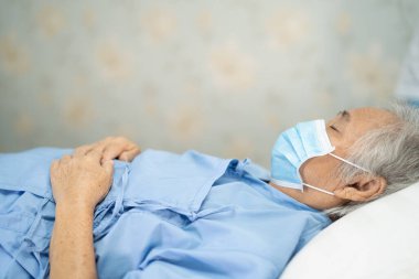Karantina hemşire hastanesi koğuşunda güvenlik enfeksiyonunu korumak için maskeyle yatan Asyalı kadın hasta Covid-19 Coronavirus salgını..