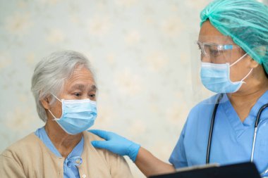 Doktor, enfeksiyon kapmasın diye hastanede yüz maskesi takan Asyalı yaşlı ya da yaşlı kadın hastaları kontrol etmek için steteskop kullanıyor..