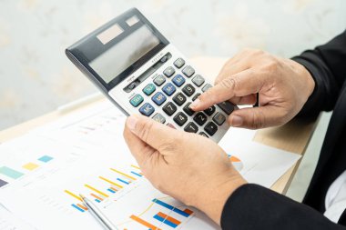 Modern ofis, finans ve iş konseptinde grafik grafik grafiği ve hesap makinesiyle çalışan ve finansal raporları analiz eden Asyalı muhasebeci.