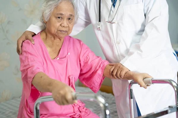 Asian nurse physiotherapist doctor care, help and support senior or elderly old lady woman patient walk with walker at hospital ward, healthy strong medical concept.