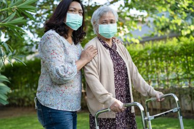 Asya 'lı yaşlı ya da yaşlı kadın Walker' la yürüyor ve güvenlik enfeksiyonu Covid-19 Coronavirus 'u korumak için maske takıyor..