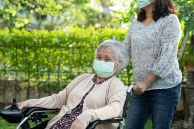 Elektrikli sandalyedeki yaşlı kadın ve yaşlı kadına yardım edin ve parktaki Covid-19 Coronavirus 'un güvenlik enfeksiyonunu korumak için maske takın..