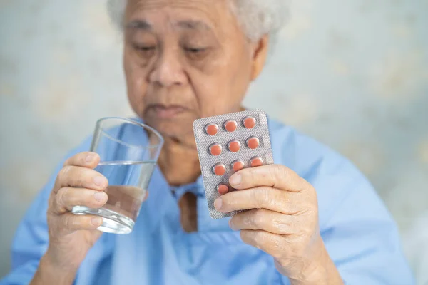 Asian senior or elderly old lady woman patient holding antibiotics capsule pills in blister packaging for treatment infection patient in hospital, Pharmacy drugstore concept.