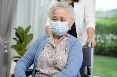 Tekerlekli sandalyede oturan ve güvenlik enfeksiyonu Covid-19 Coronavirus 'u korumak için maske takan yaşlı kadına yardım edin..