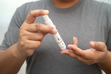 Evde parmak üzerinde dijital mızrakla kan şekeri seviyesini ölçmek için Asyalı kadın kendini test ediyor..