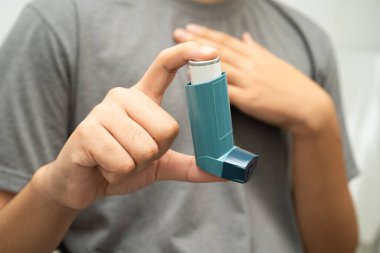 Astım ve kronik obstrüktif akciğer hastalığı COPD, Asyalı genç adam ölçülü doz solunum cihazı kullanıyor..