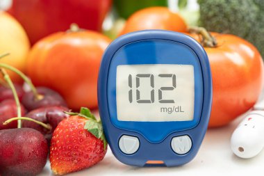 Asya 'da el ele tutuşan dijital glikoz monitörü sebze ve meyveli sağlıklı gıda ölçümü.