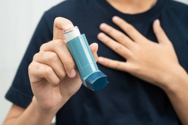 Astım ve kronik obstrüktif akciğer hastalığı COPD, Asyalı genç adam ölçülü doz solunum cihazı kullanıyor..