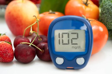 Asya 'da el ele tutuşan dijital glikoz monitörü sebze ve meyveli sağlıklı gıda ölçümü.