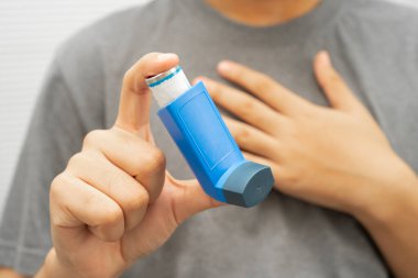 Astım ve kronik obstrüktif akciğer hastalığı COPD, Asyalı genç adam ölçülü doz solunum cihazı kullanıyor..