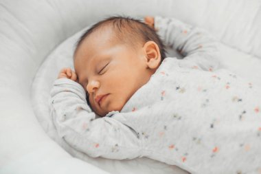 Beyaz giysiler içinde uyuyan beyaz bir bebeğin üst görünüm fotoğrafı.