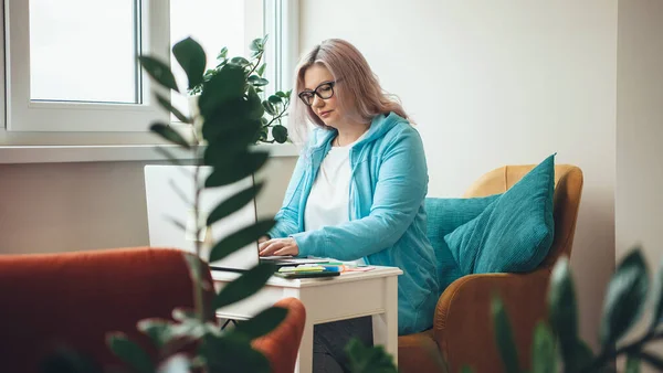 Upptagen kaukasiska senior affärskvinna med glasögon använder en bärbar dator hemma medan du arbetar på distans — Stockfoto