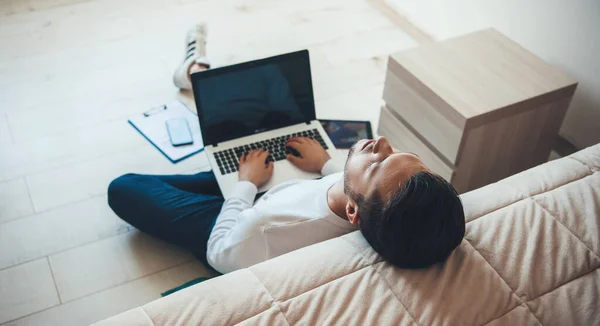 Jovem homem de negócios caucasiano sentindo-se cansado depois de trabalhar no laptop de casa sentado no chão perto da cama adormecer — Fotografia de Stock