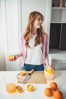 Çilli güzel kızıl kadın, portakal dilimlerken gülümsüyor manuel sıkma makinesiyle meyve suyu yaptığı için.