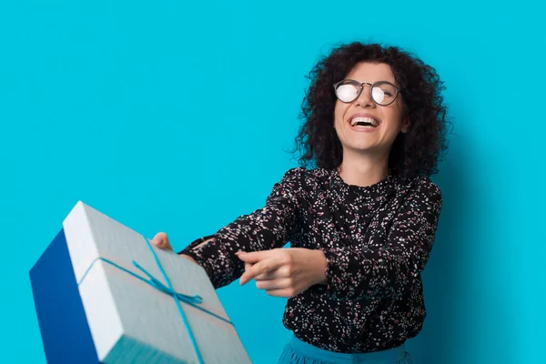 Preciosa mujer de pelo rizado está sonriendo a la cámara y recibir un regalo en una pared de estudio azul —  Fotos de Stock