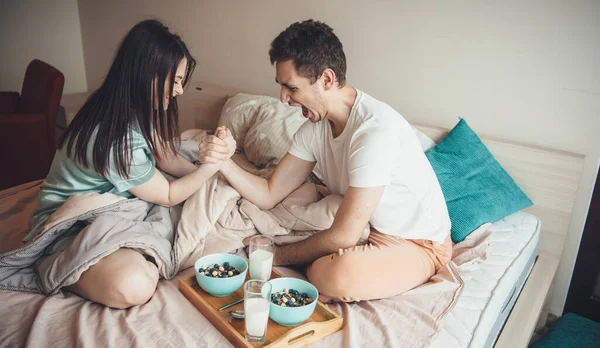 Lovely caucasian couple are playing in bed before eating cereals with milk feeling happy and measuring their power — Stock Photo, Image