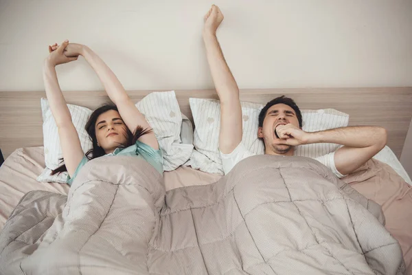 白种人夫妇在床上打呵欠，早上躺在被子上伸懒腰 — 图库照片