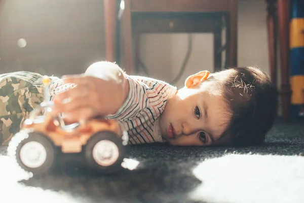 Garoto caucasiano deitado no chão e brincando com um carro de brinquedo durante um dia ensolarado — Fotografia de Stock