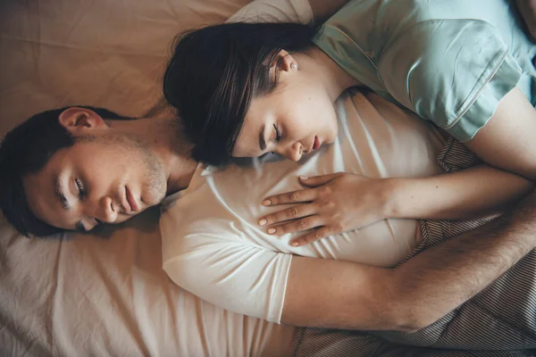 Brunette caucasian woman is sleeping on her boyfriend chest relaxing together in bed covered with a quilt — Stock Photo, Image
