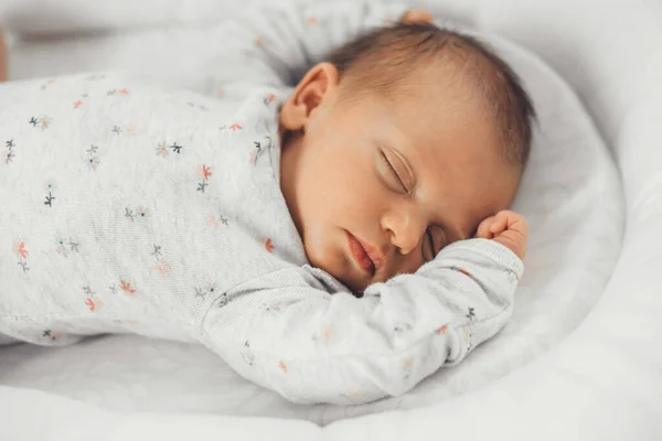 Close up photo of a sleeping baby in warm clothes with black hair feeling safe in his own bed