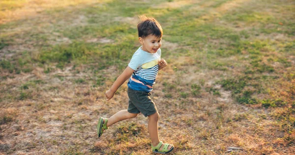 Бегущий кавказский мальчик улыбается на зеленом поле в парке во время летней прогулки — стоковое фото