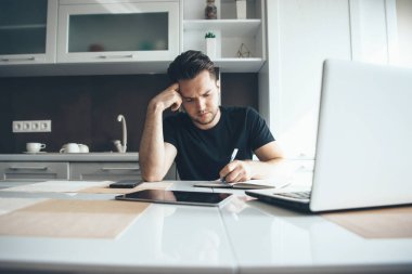 Genç işadamı mutfaktaki evden bilgisayarla bir şeyler yazarken uzaktan çalışıyor.