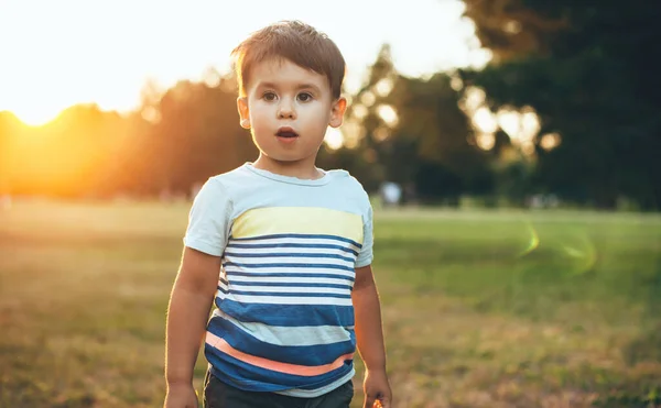Adorável menino caucasiano posando em roupas casuais em um campo com um pôr do sol no fundo — Fotografia de Stock