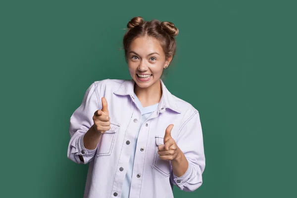 Blonde Frau lächelt und zeigt in Jeanskleidung auf eine grüne Studiowand — Stockfoto
