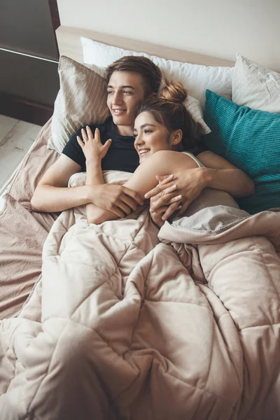 Φωτογραφία πάνω όψης ενός καυκάσιου ζευγαριού ξαπλωμένου στο κρεβάτι αγκαλιασμένο κάτω από μια κουβέρτα και χαμογελώντας σε ένα πρωινό — Φωτογραφία Αρχείου