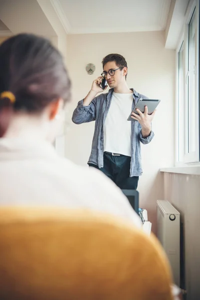 Volver ver foto de una mujer caucásica sentada en una silla mientras su socio de negocios está hablando por teléfono con una tableta en la mano — Foto de Stock