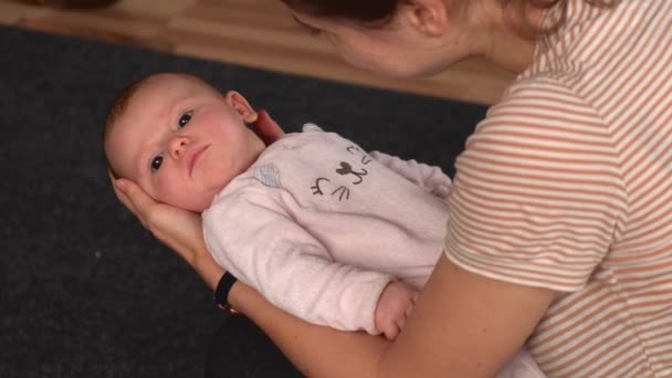 Blanke moeder in casual kleding houdt haar pasgeboren meisje in de handen en zwaait haar in slaap terwijl ze vrolijk glimlacht — Stockvideo