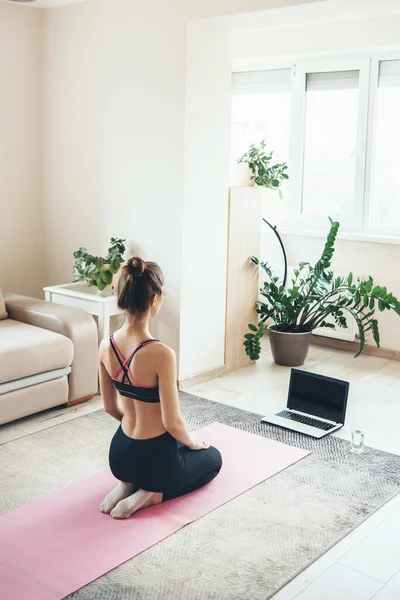 Donna sportiva caucasica in abbigliamento sportivo sta guardando il computer portatile sul pavimento durante la lezione di yoga online — Foto Stock