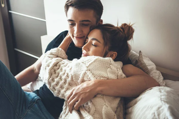 Mujer caucásica en suéter de punto blanco está abrazando a su amante mientras está acostada en la cama y sonríe —  Fotos de Stock