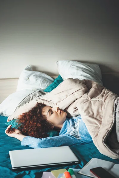 Cansada mujer caucásica con el pelo rizado relajante después de hacer la tarea en el portátil en la cama —  Fotos de Stock