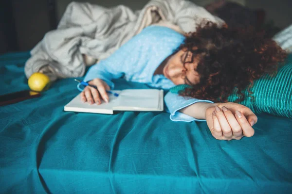 Caucásica mujer acostada somnolienta en la cama está leyendo algo de un libro con pijama azul tarde por la noche — Foto de Stock