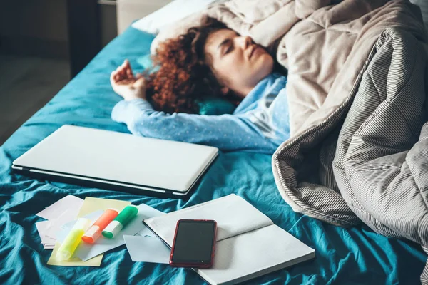 Femme caucasienne aux cheveux bouclés portant un pyjama bleu dort après avoir fait ses devoirs jusqu'à la nuit avec un ordinateur portable — Photo