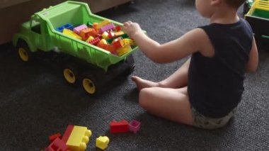 Kafkasyalı bir çocuğun inşaat malzemelerini toplarken ve yerde oynarken arabaya koyarkenki görüntüsü.
