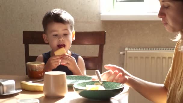 Caucasien garçon est manger cookies tandis que son taches de rousseur mère est manger céréales avec bananes — Video