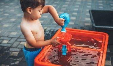 Göbeği açık beyaz çocuk su ve plastik oyuncaklarla oynuyor.