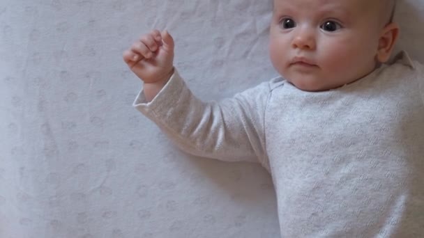 Οι γονείς κινηματογραφούν το νεογέννητο κοριτσάκι τους ξαπλωμένο σε λευκή κουβέρτα και κοιτώντας την κάμερα να κουνάει τα χέρια. — Αρχείο Βίντεο