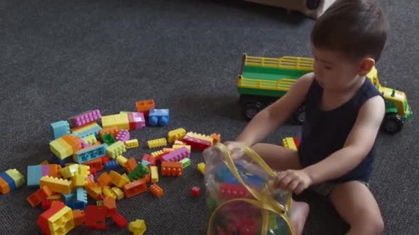 Vit pojke rengör golvet efter att ha lekt med konstruktörer bitar samla dem i en stor leksak väska — Stockvideo