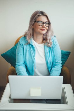 Dizüstü bilgisayarın başında çalışırken gülümseyen yaşlı sarışın bir kadının ön görüntüsü.