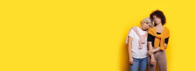 Çekici sarışın kadın, başını kız kardeşlerinin omuzlarına koyuyor üzgün hissediyor ve sarı bir stüdyo duvarında poz veriyor.