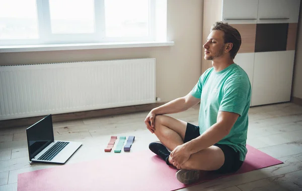 Bionda caucasico uomo sta meditando sul pavimento utilizzando un computer portatile e elastici — Foto Stock