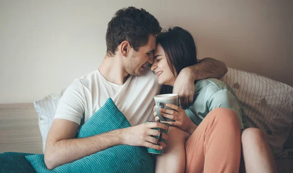 Kaukaska para obejmująca się w łóżku podczas picia razem kawy uśmiechnięta — Zdjęcie stockowe
