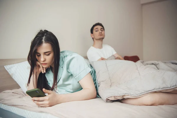 Celoso hombre caucásico está tratando de mirar quién es su novia escribiendo, usando un teléfono en la cama — Foto de Stock