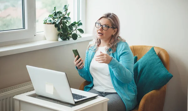 Busy senior woman with blonde hair and glasses is having online meeting o laptop working from home — Stock Photo, Image