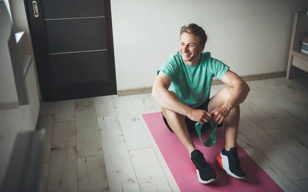 Hombre sonriente con cabello rubio usando ropa deportiva en el suelo durante una clase de fitness en casa — Foto de Stock