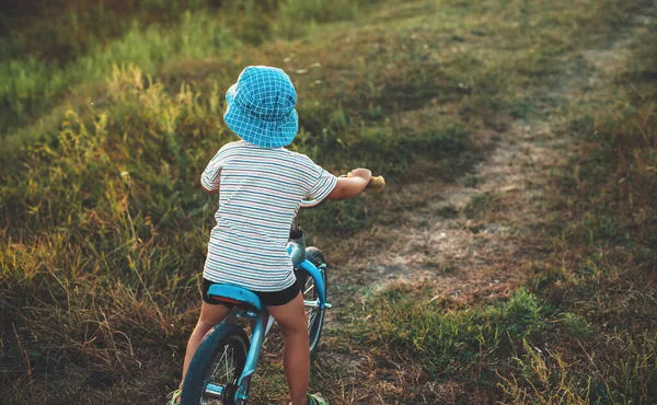 Arka planda mavi şapkalı beyaz bir çocuğun tarlada bisiklete binerken fotoğrafı var. — Stok fotoğraf