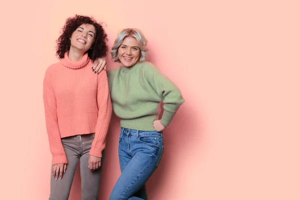 Monochromes Foto von zwei Frauen mit lockigem Haar, die an einer Studiowand posieren und dabei in die Kamera lächeln — Stockfoto